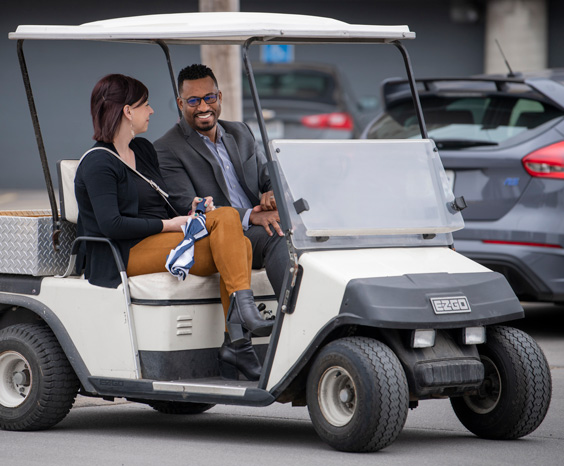Two Blue KC Customer Experience team members driving in a golf cart and smiling.