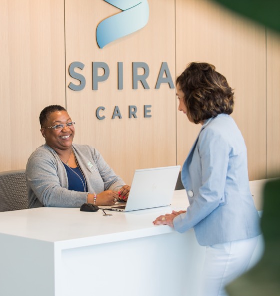 Woman behind check-in counter with a computer helps a customer at Spira Care